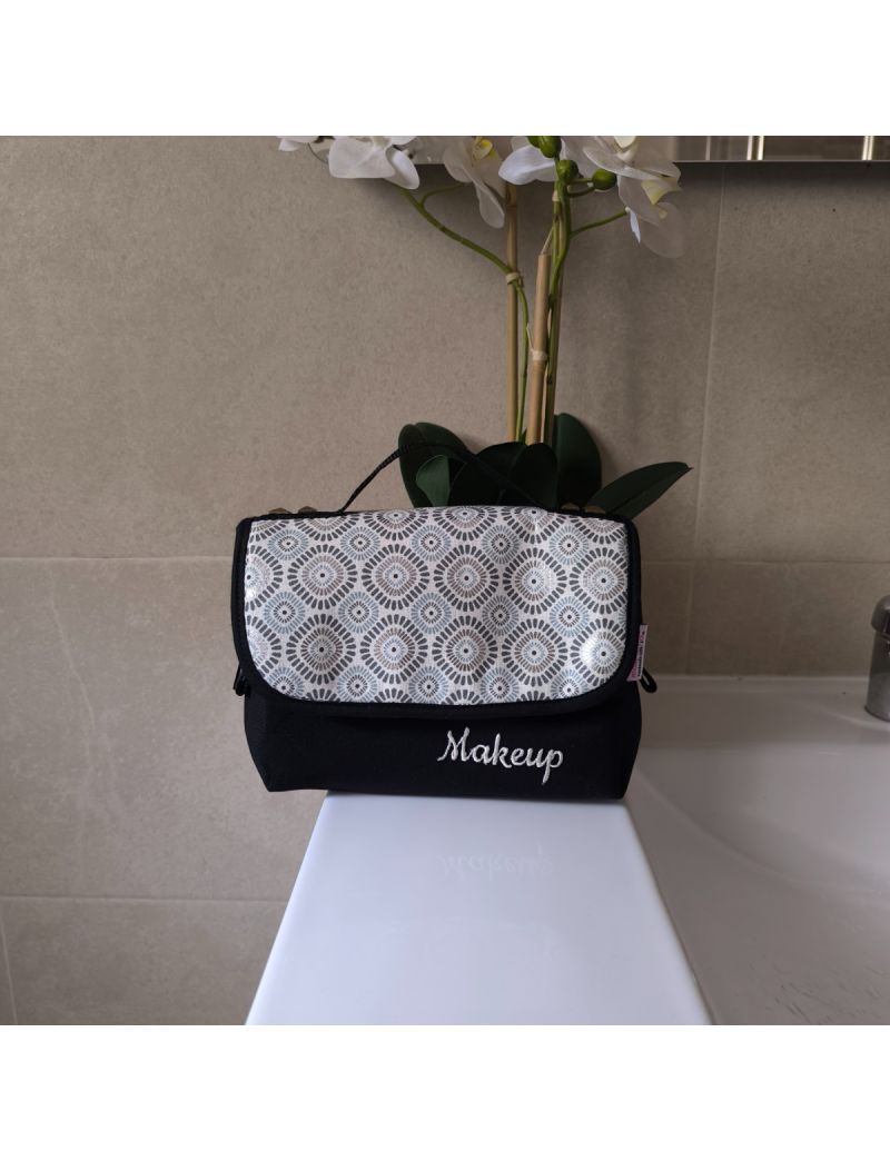 
Bolsa de maquilhagem fechada, compacta com padr&atilde;o geom&eacute;trico, cinza, preto e prateado, colocada sobre uma bancada de casa de banho.
