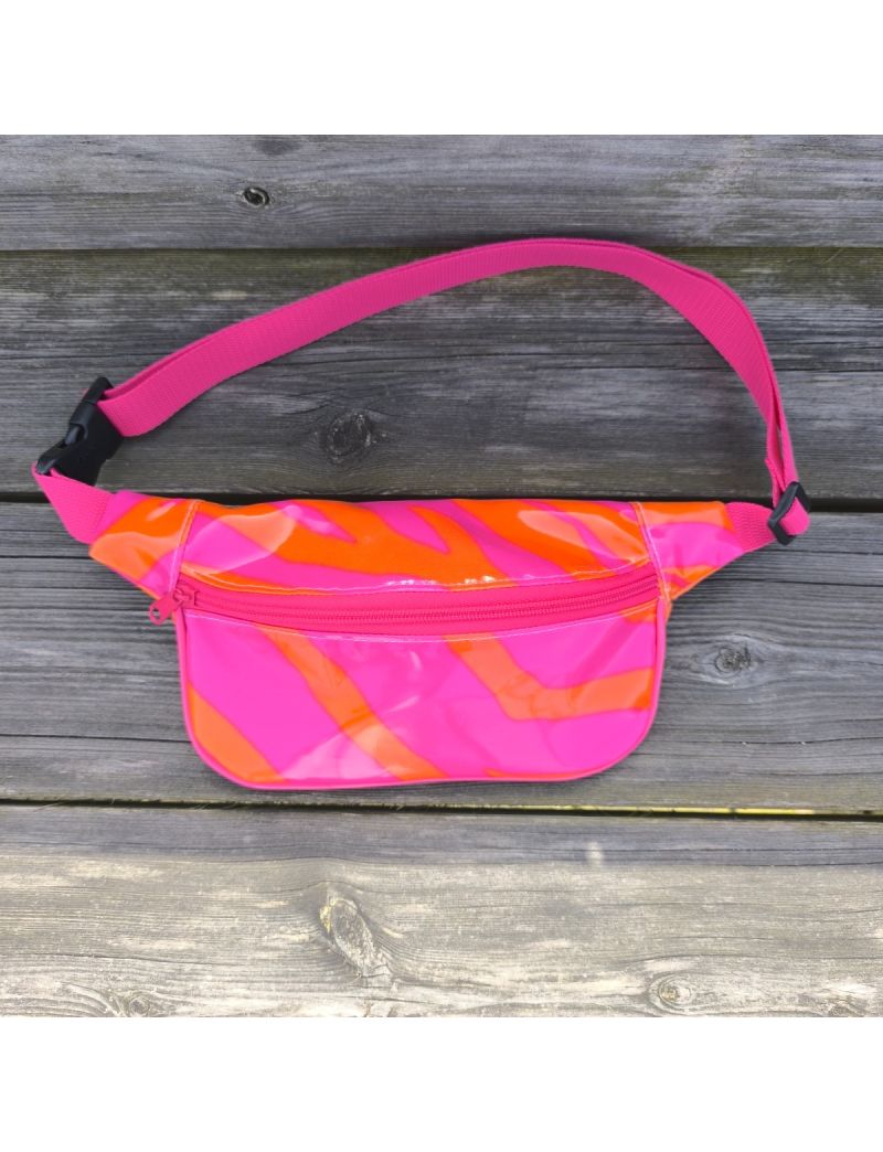 Bolsa de cintura com acabamento brilhante em padr&atilde;o zebra neon, alternando listas rosa choque e laranja vibrante. Possui fecho de correr rosa, al&ccedil;a ajust&aacute;vel em rosa com fivela preta, e est&aacute; pousada sobre um banco de madeira r&uacute;stica