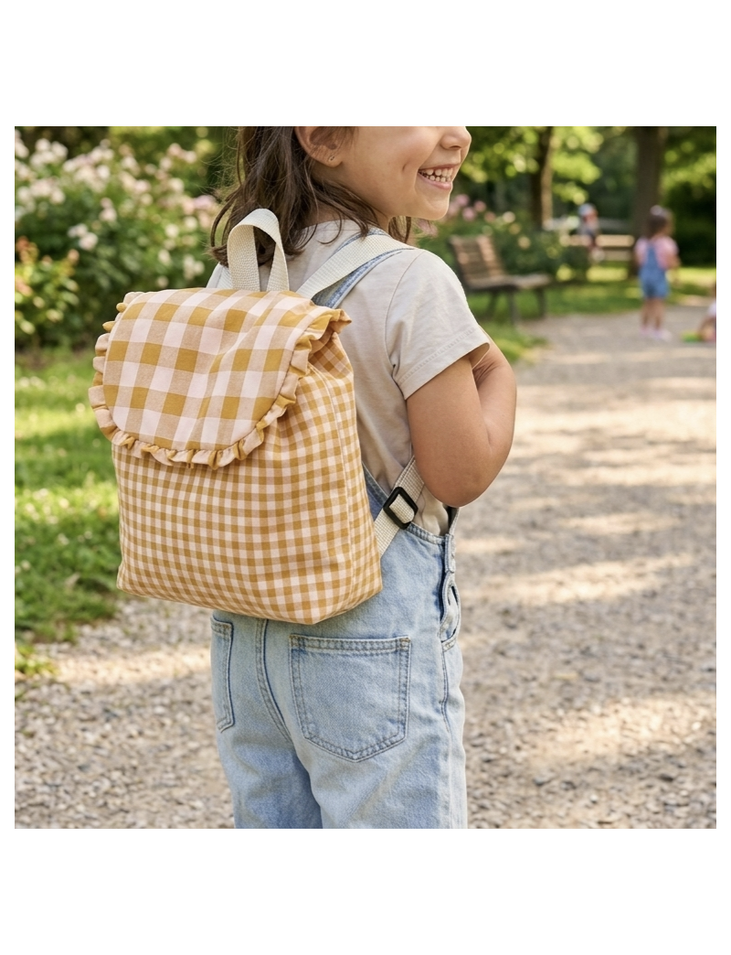 Menina com mochila colocada. Em tecido vicky amarelo torrado m&eacute;dio e grande na pala, folho na pala. Com al&ccedil;as na cor p&eacute;rola 
