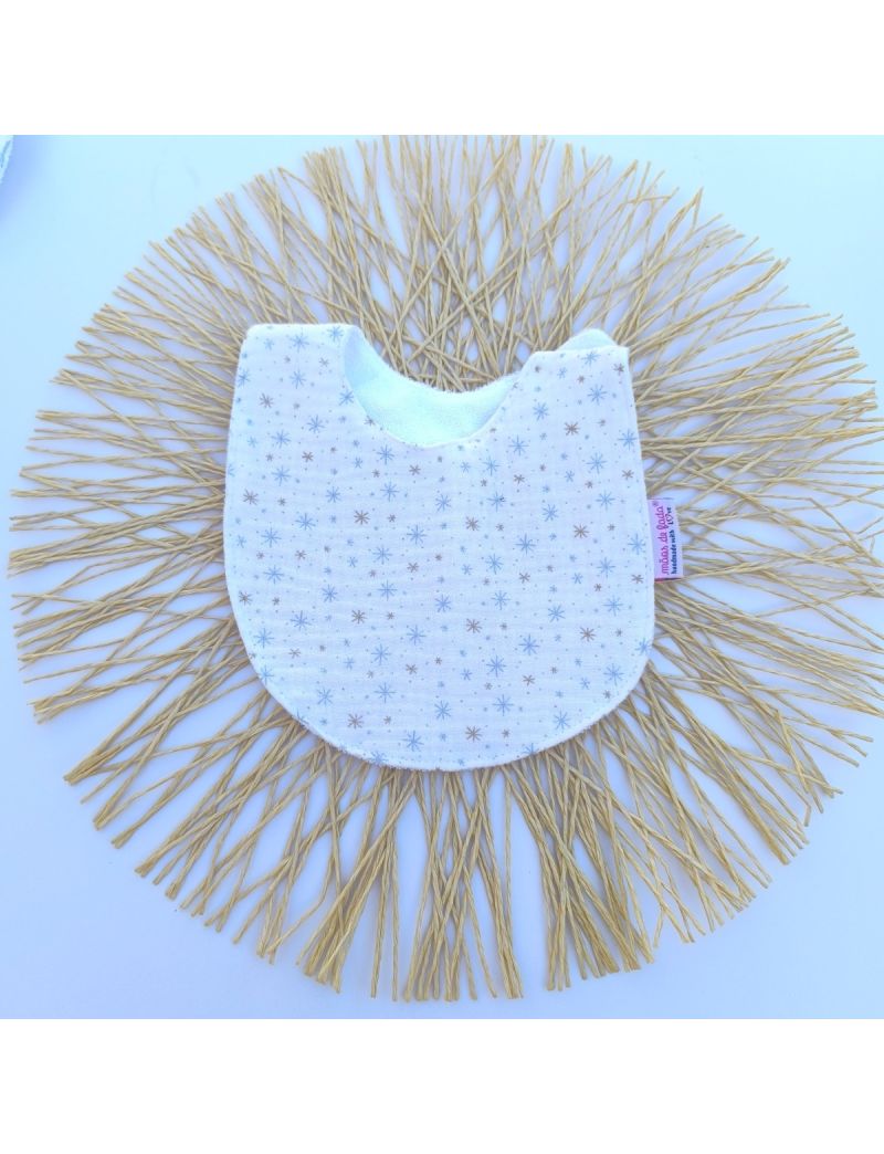 Babete de mola infantil com corte arredondado, feito em musselina org&acirc;nica branca e macia. O tecido exibe um padr&atilde;o impresso composto por pequenas estrelas estilizadas e pontos brilhantes em tons de azul-claro e bege.