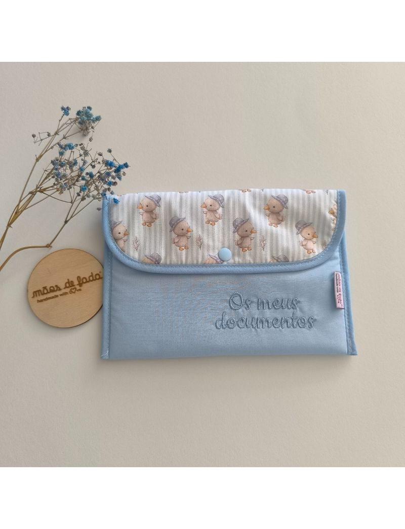 Porta documentos em formato envelope com padrão azul liso com pala com padrão de pintainhos, com a inscrição "Os meus documentos" bordado a azul