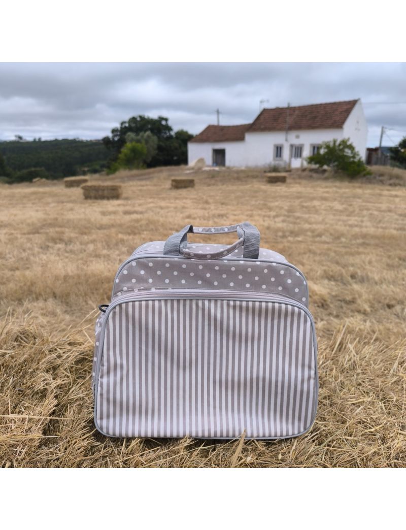 Perspetiva frontal da lancheira. Cinzenta com bolas brancas e bolso frontal com riscas cinza e brancas. Fecho e alças em cinzento