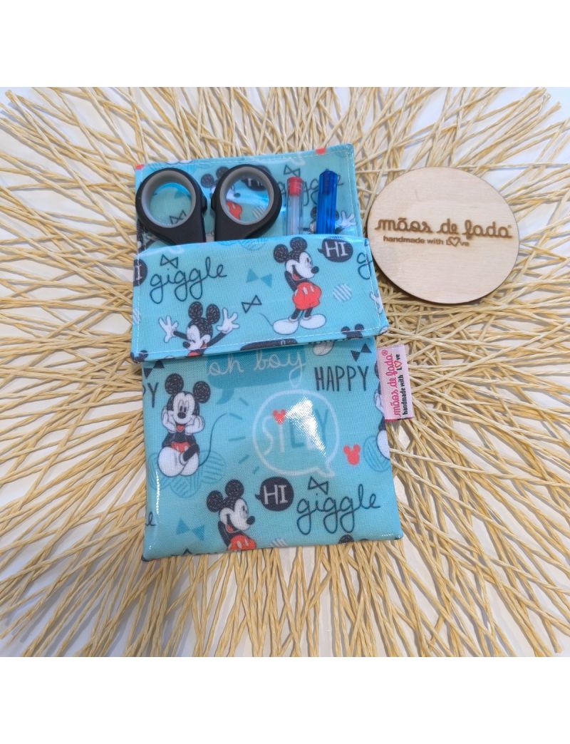 Bolsa para bata plastificada com padrão do Mickey, contendo canetas e tesoura, ao lado de um logótipo em madeira  com a designação “mãos de fada handmade with love”