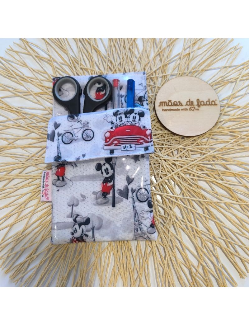 Bolsa para bata plastificada com padrão do Mickey e Minnie, contendo canetas e tesoura, ao lado de um logótipo em madeira  com a designação “mãos de fada handmade with love”