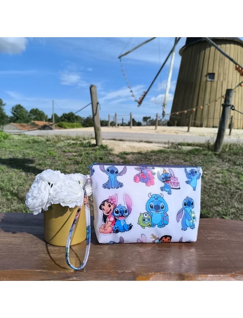 Necessaire em tecido plastificado com padrão Lilo & Stitch, colocada sobre banco de madeira com flores brancas decorativas e moinho ao fundo, em ambiente ao ar livre.