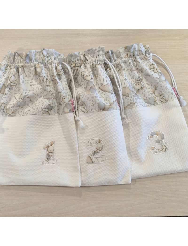 Conjunto de tr&ecirc;s taleigos de maternidade em tons de branco e bege, numerados de 1 a 3. A parte superior apresenta um padr&atilde;o de coelhinhos e bal&otilde;es em tons neutros, enquanto a parte inferior &eacute; em piquet branco. Cada saco tem um cord&atilde;o de fecho branco e num