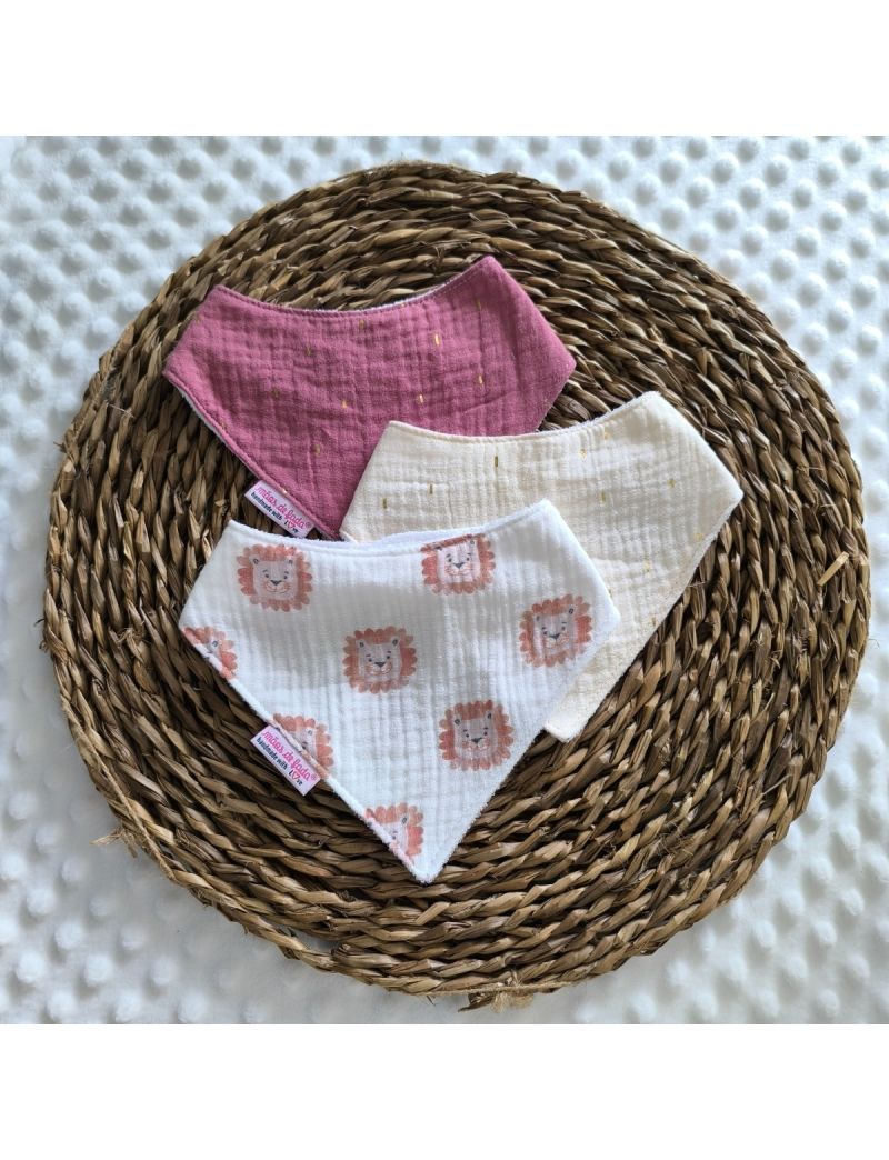 Conjunto de tr&ecirc;s babetes badana em musselina dispostos sobre uma base de verga circular. O pack apresenta um babete central p&eacute;rola ccom apontamenos dourados, ladeado por dois babetes; um com le&otilde;es e outro de tom beringela