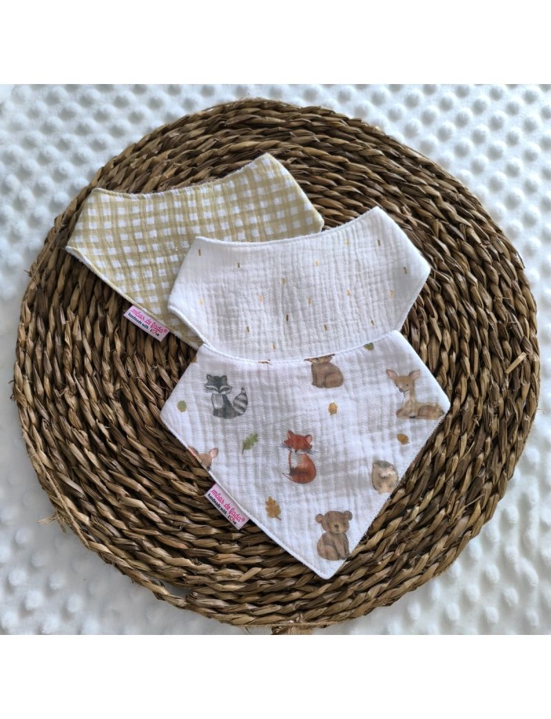 Conjunto de tr&ecirc;s babetes badana em musselina dispostos sobre uma base de verga circular. O pack apresenta um babete central branco com apontamentos dourados, ladeado por dois babetes; um com ilustra&ccedil;&otilde;es de raposas, veados e esquilos e outro em vicky amare