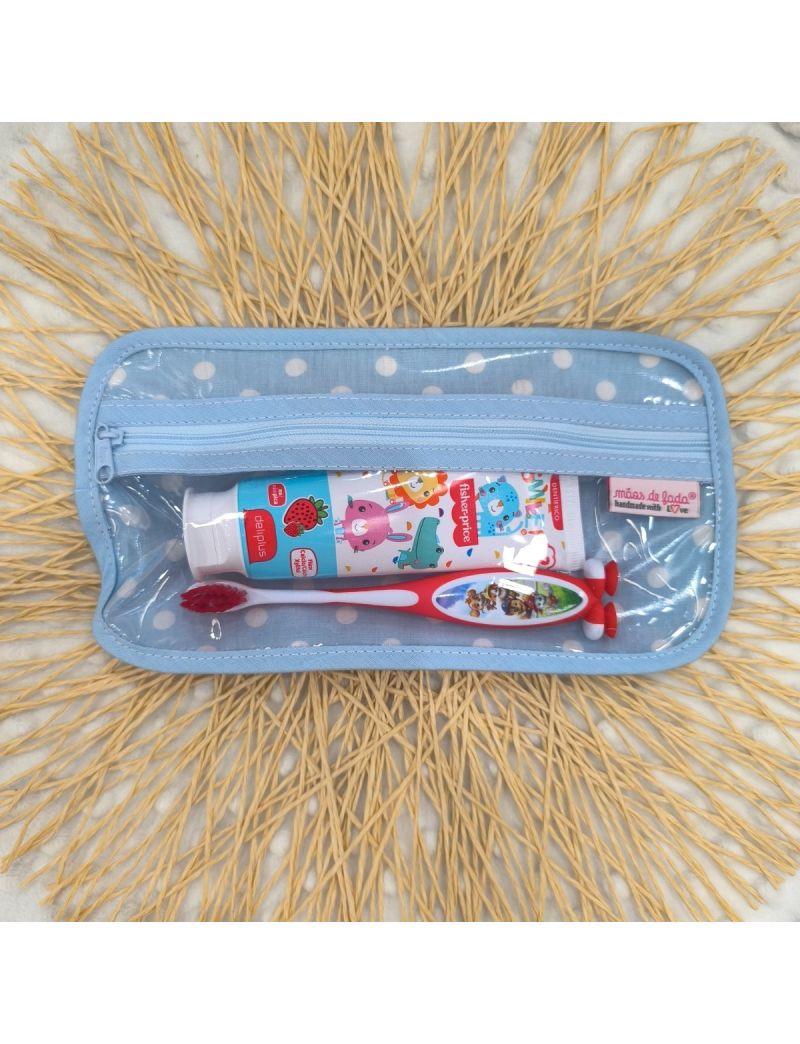 Bolsa de higiene para crian&ccedil;a com fundo azul claro e bolas brancas. Fecho azul claro. No interior possui uma escova e pasta de dentes como exemplo